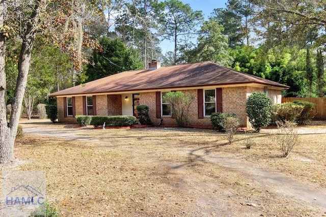 ranch-style house featuring brick siding, a chimney, and fence