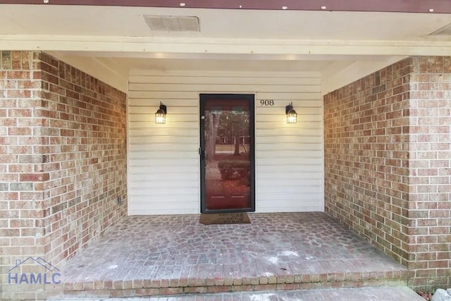 view of exterior entry with visible vents, a porch, and brick siding