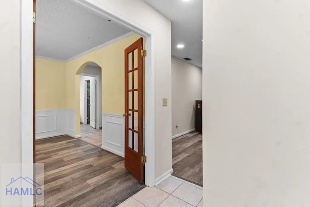 hallway featuring arched walkways, wainscoting, wood finished floors, and crown molding