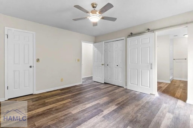 unfurnished bedroom featuring a barn door, baseboards, a ceiling fan, wood finished floors, and a closet