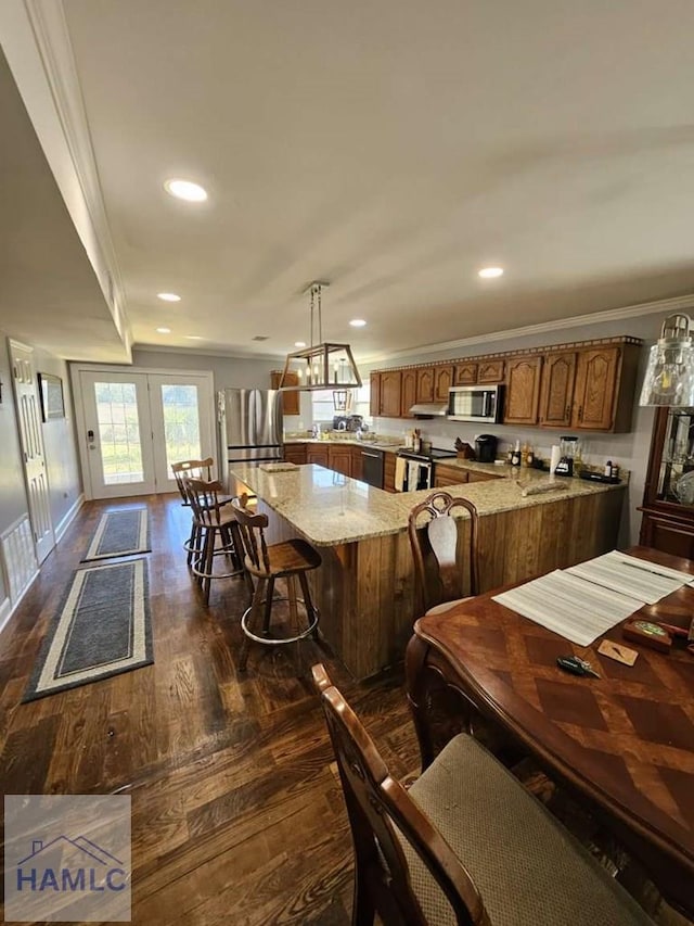 kitchen with stainless steel appliances, light stone countertops, pendant lighting, and ornamental molding