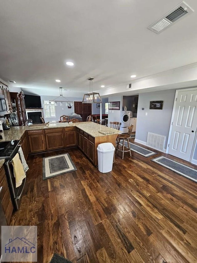 kitchen featuring kitchen peninsula, appliances with stainless steel finishes, light stone countertops, washer / dryer, and hanging light fixtures