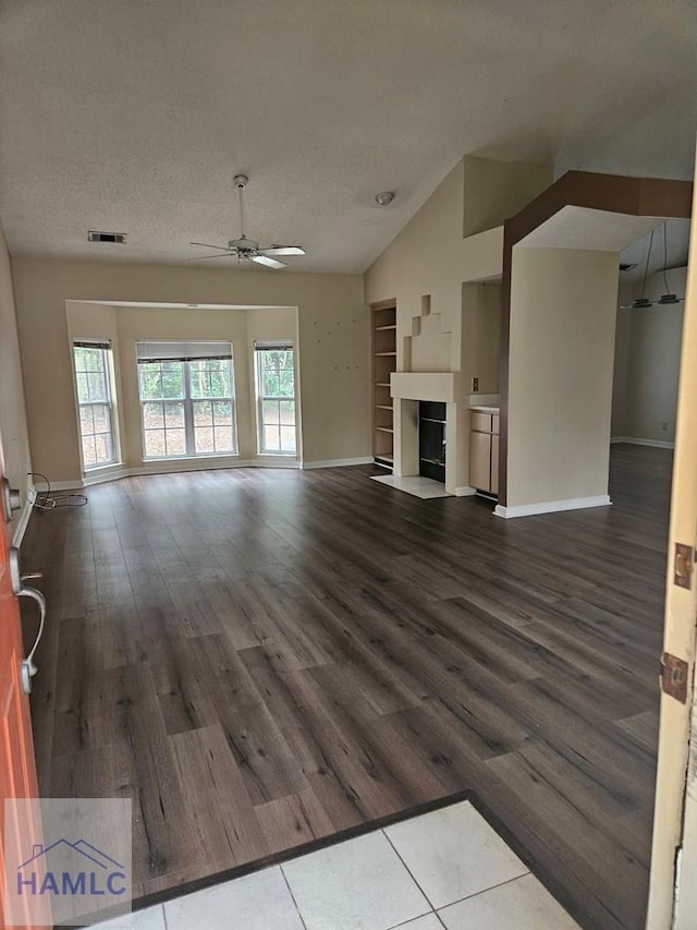 unfurnished living room with a textured ceiling, lofted ceiling, dark hardwood / wood-style flooring, built in features, and ceiling fan