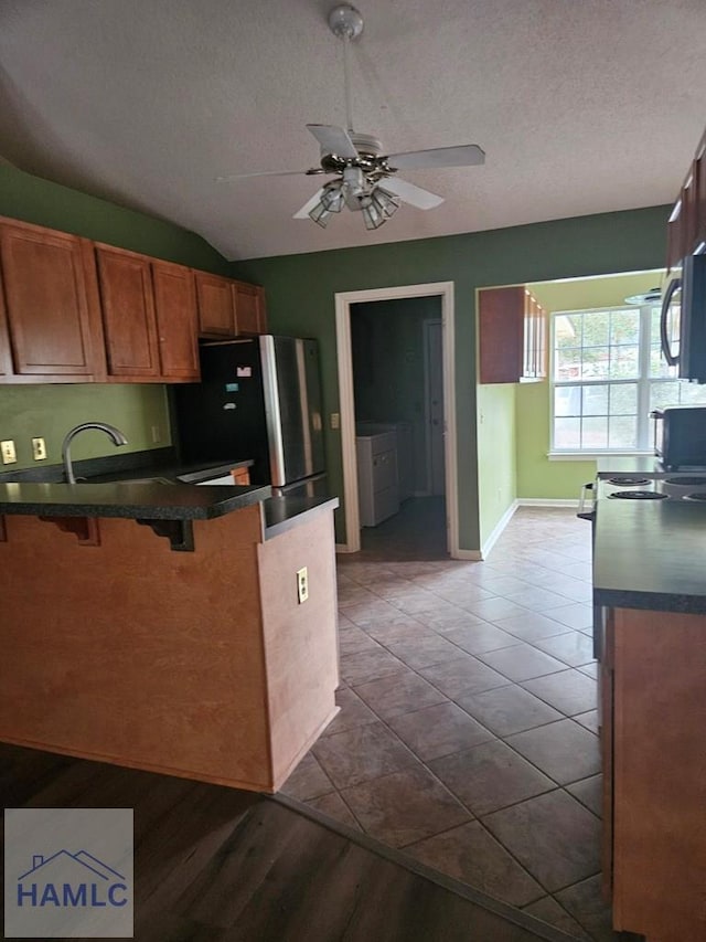 kitchen with a textured ceiling, vaulted ceiling, a kitchen breakfast bar, ceiling fan, and stainless steel fridge