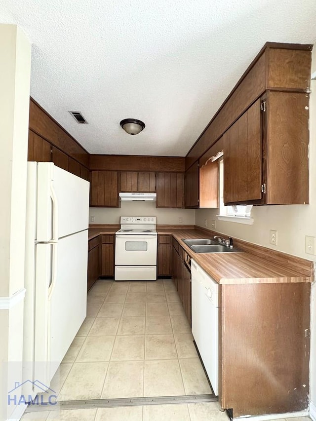 kitchen with dark brown cabinets, a textured ceiling, white appliances, sink, and light tile patterned floors