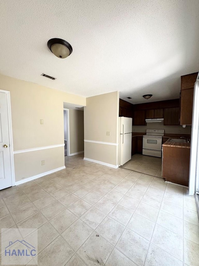 interior space featuring dark brown cabinets, light tile patterned flooring, white appliances, and a textured ceiling