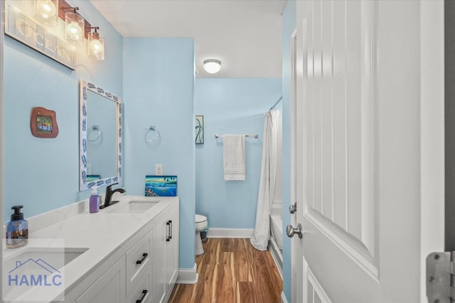 full bath with baseboards, double vanity, toilet, wood finished floors, and a sink
