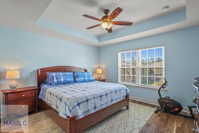 bedroom featuring a ceiling fan, a raised ceiling, baseboards, and wood finished floors