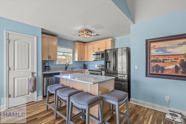 kitchen with a breakfast bar area, stainless steel appliances, light brown cabinetry, a center island, and a sink