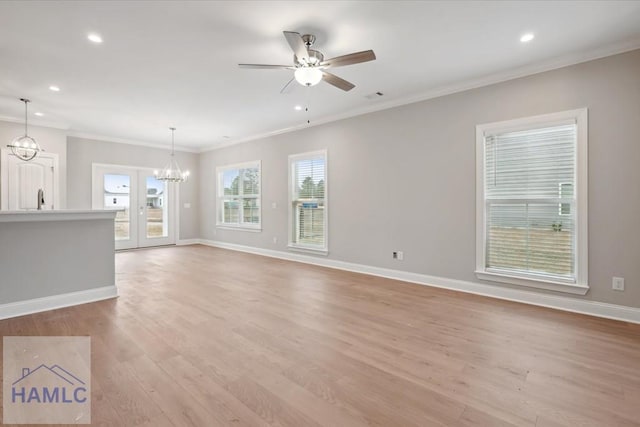 unfurnished living room with sink, crown molding, ceiling fan with notable chandelier, and light wood-type flooring