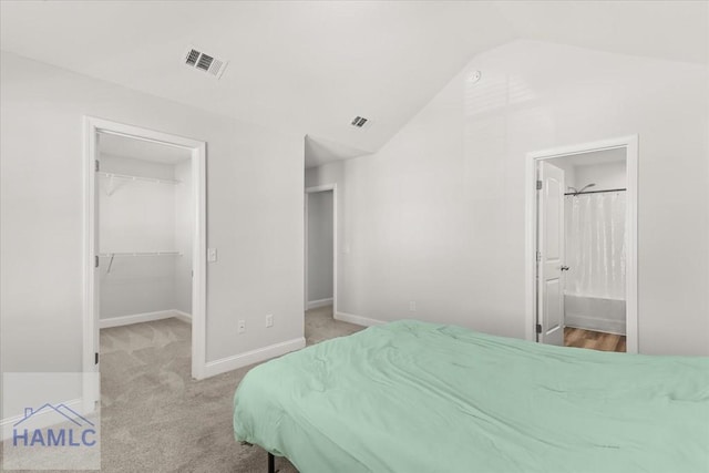 bedroom featuring a walk in closet, a closet, baseboards, light colored carpet, and vaulted ceiling