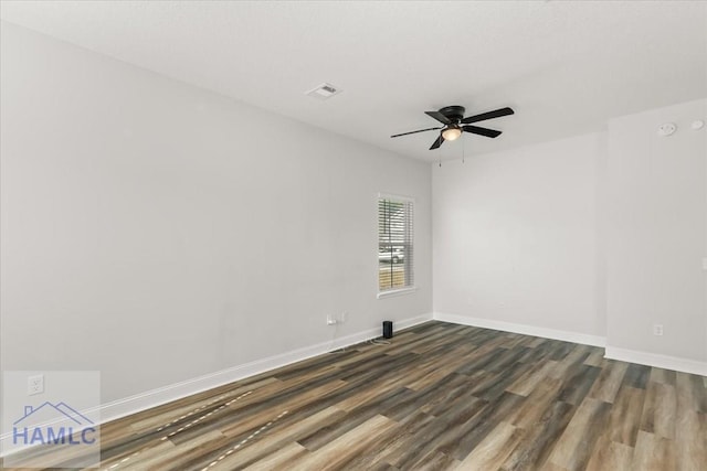 spare room featuring visible vents, a ceiling fan, dark wood-type flooring, and baseboards