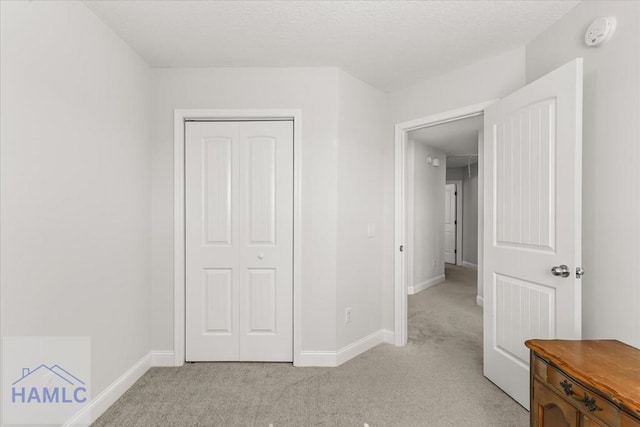 unfurnished bedroom with a closet, light colored carpet, a textured ceiling, and baseboards