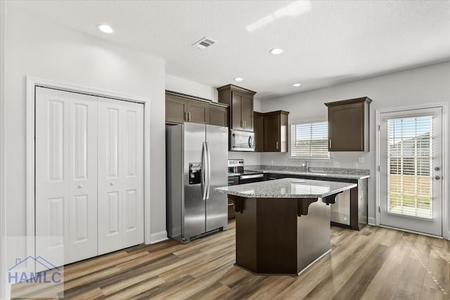 kitchen featuring light wood-type flooring, stainless steel appliances, dark brown cabinetry, and visible vents