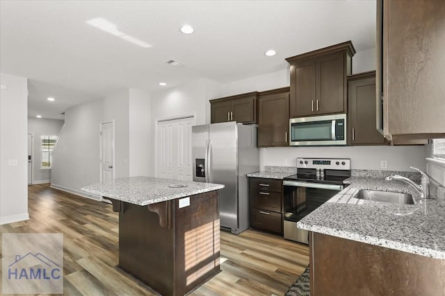 kitchen with a sink, a center island, appliances with stainless steel finishes, light wood finished floors, and dark brown cabinets