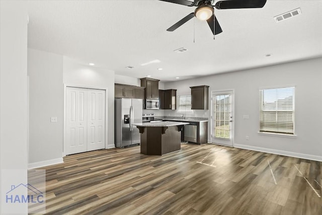 kitchen featuring visible vents, a kitchen island, dark brown cabinetry, appliances with stainless steel finishes, and a kitchen bar