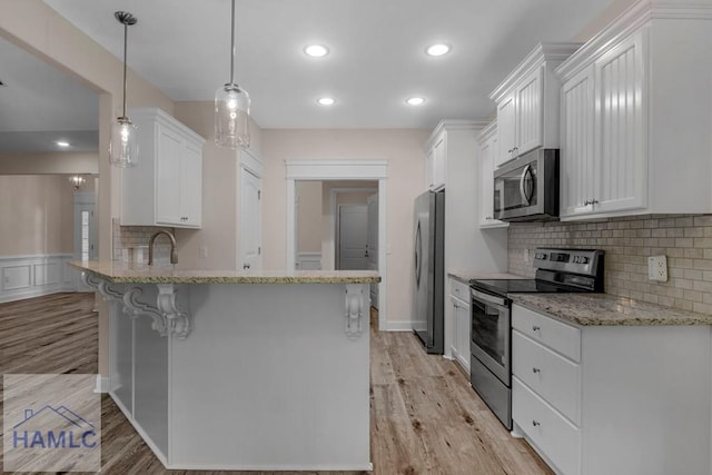 791 Stafford Dairy Rd SE, Ludowici, GA 31316 - kitchen with stainless steel appliances, a breakfast bar, light wood finished floors, white cabinets, and a peninsula