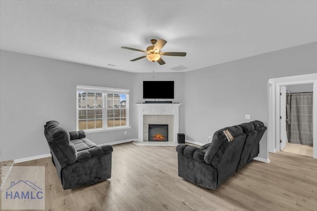 living room featuring a tile fireplace, ceiling fan, and light hardwood / wood-style flooring