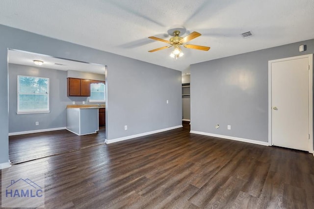 unfurnished living room featuring ceiling fan, dark wood-type flooring, and a textured ceiling