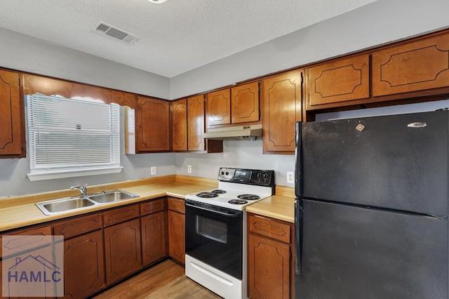 kitchen with white range with electric cooktop, black refrigerator, sink, light wood-type flooring, and a textured ceiling