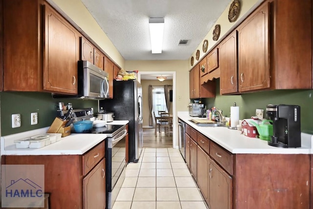 1267 Louise Ln, Hinesville, GA 31313 - kitchen featuring stainless steel appliances, a textured ceiling, light tile patterned floors, light countertops, and brown cabinetry
