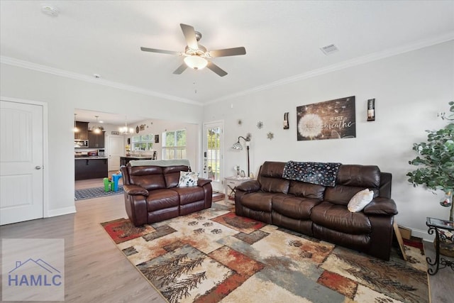 living room featuring crown molding, ceiling fan with notable chandelier, baseboards, wood finished floors, and visible vents