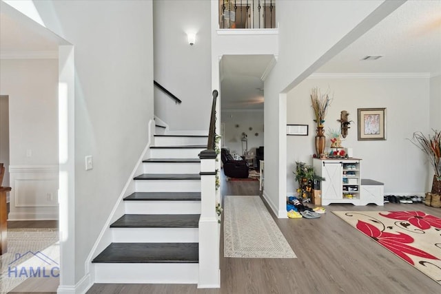 stairway with crown molding, wood finished floors, and visible vents