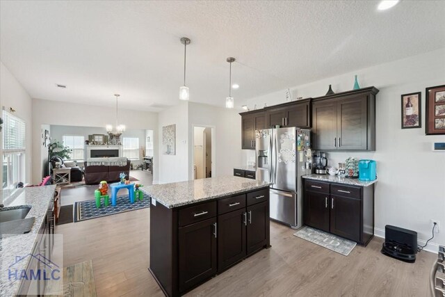 kitchen featuring stainless steel refrigerator with ice dispenser, light wood finished floors, a notable chandelier, and light stone countertops