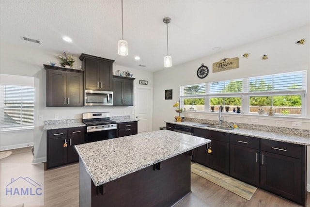 kitchen featuring visible vents, a center island, light stone counters, a sink, and appliances with stainless steel finishes