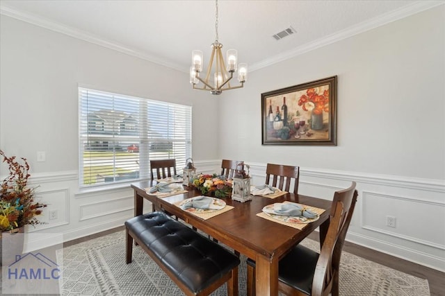 dining room featuring visible vents, ornamental molding, wood finished floors, a wainscoted wall, and a notable chandelier