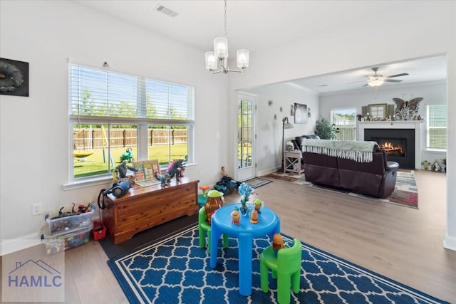 rec room with visible vents, wood finished floors, baseboards, a lit fireplace, and ceiling fan with notable chandelier