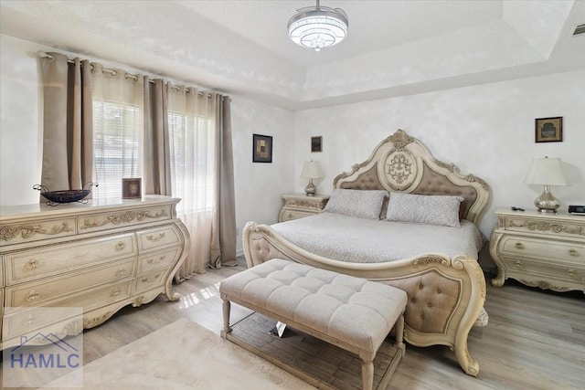 bedroom with a tray ceiling and light wood-type flooring