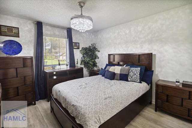 bedroom featuring a chandelier, a textured ceiling, and light hardwood / wood-style flooring