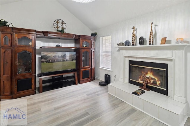 living room featuring high vaulted ceiling, light wood-type flooring, and a tile fireplace