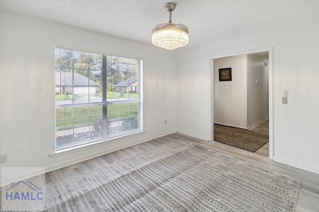 empty room featuring a chandelier, a textured ceiling, and light wood-type flooring