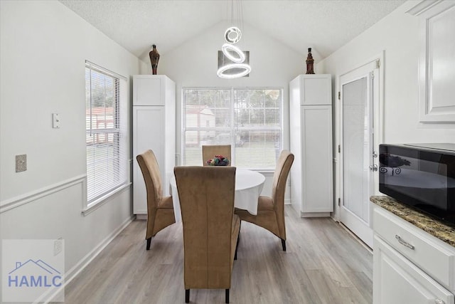 dining room featuring a textured ceiling, light hardwood / wood-style flooring, and lofted ceiling