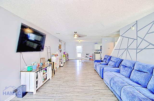 living room with ceiling fan, a textured ceiling, and light hardwood / wood-style floors