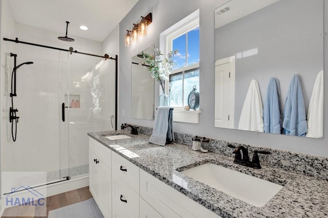 bathroom featuring double vanity, visible vents, a stall shower, and a sink