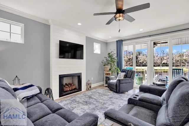 living area with a large fireplace, baseboards, ceiling fan, ornamental molding, and wood finished floors