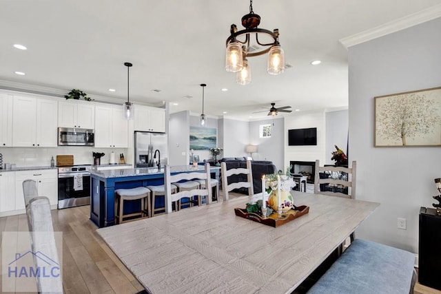 dining area with light wood-type flooring, ornamental molding, recessed lighting, a fireplace, and ceiling fan