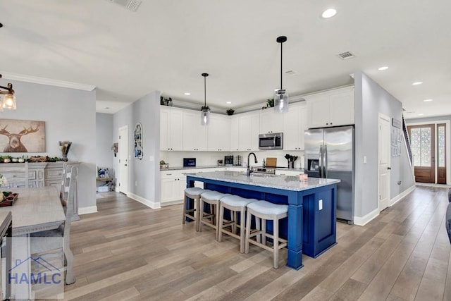 kitchen with light stone countertops, light wood-style floors, white cabinets, stainless steel appliances, and a sink