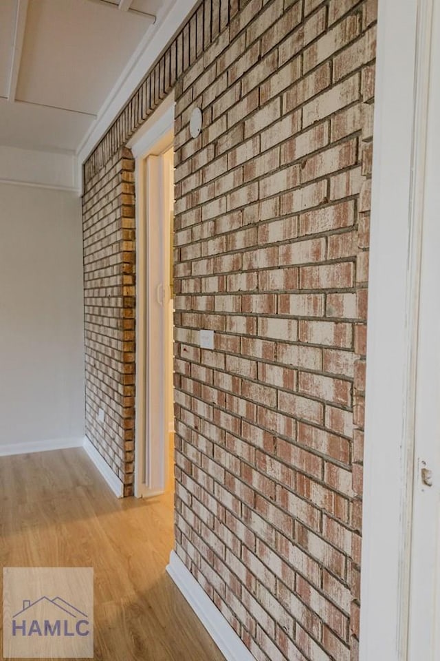 corridor with light wood-type flooring and brick wall