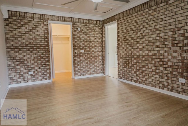 spare room featuring ceiling fan, light wood-type flooring, and brick wall