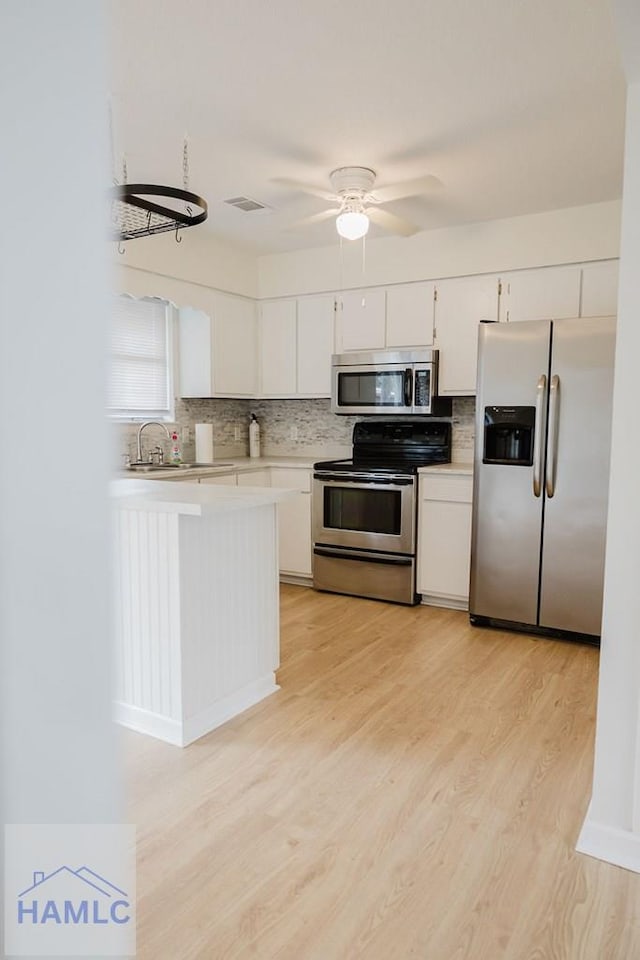 kitchen featuring white cabinets, decorative backsplash, ceiling fan, light wood-type flooring, and stainless steel appliances