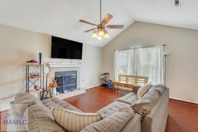 living room with dark hardwood / wood-style floors, a tiled fireplace, vaulted ceiling, and a textured ceiling