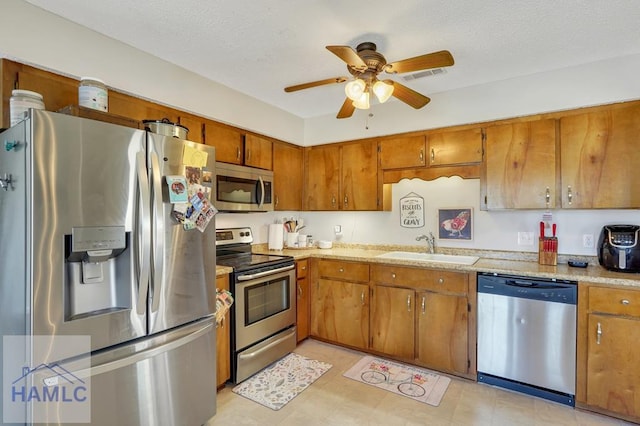 kitchen featuring light stone countertops, appliances with stainless steel finishes, sink, and ceiling fan