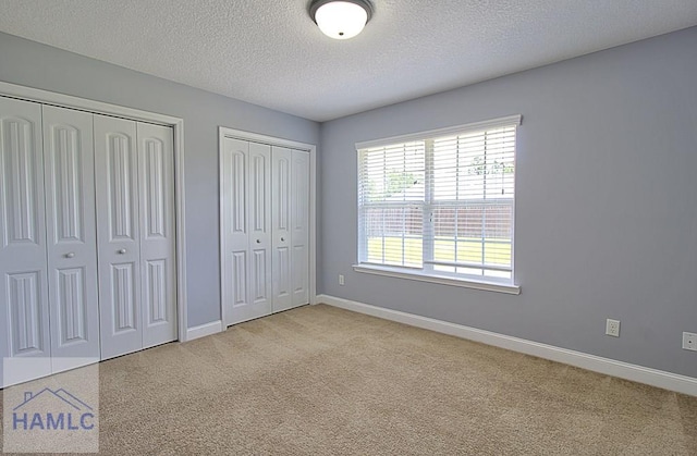 unfurnished bedroom with a textured ceiling, light carpet, and two closets