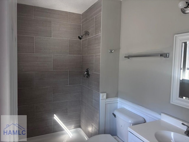 bathroom with toilet, tiled shower, and vanity