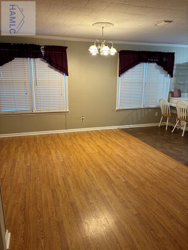 unfurnished dining area featuring hardwood / wood-style flooring, ornamental molding, and a chandelier