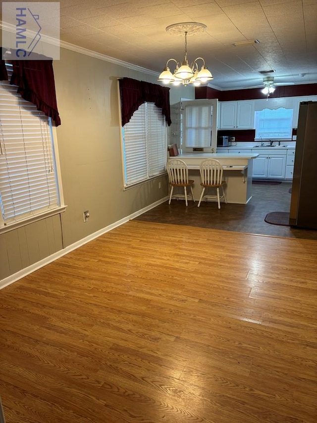 unfurnished dining area featuring ceiling fan with notable chandelier, sink, hardwood / wood-style flooring, and crown molding